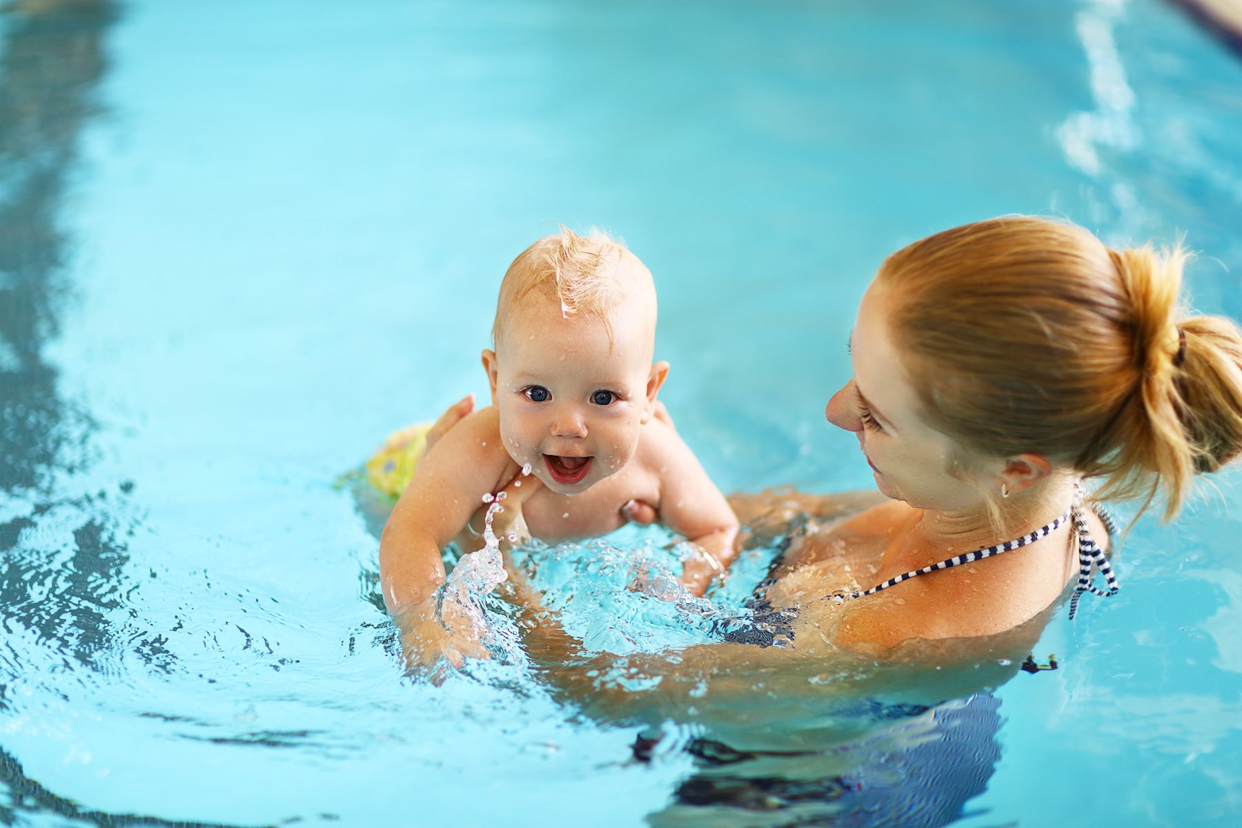 mother teaching baby swimming pool